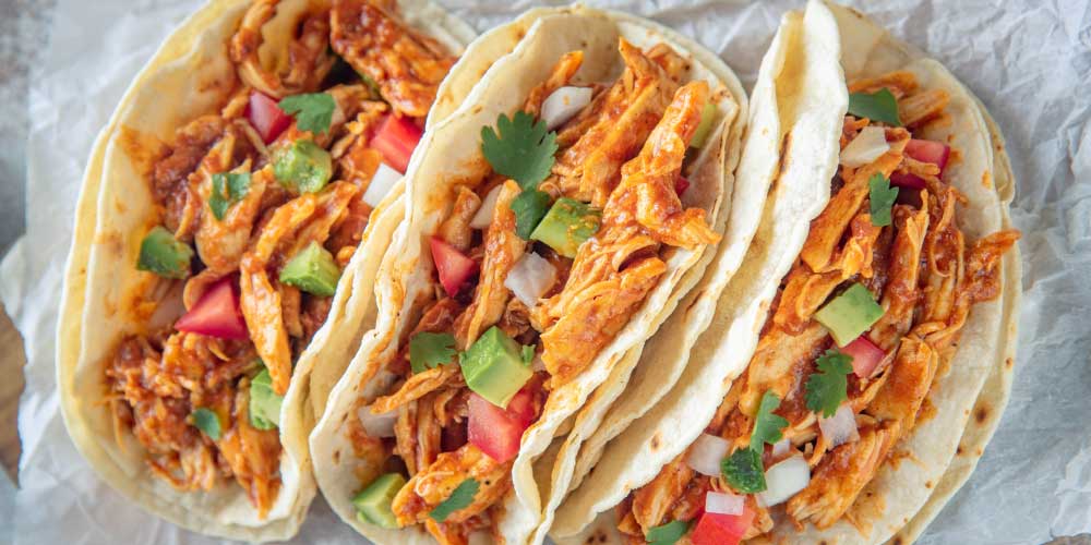 Three soft tacos filled with barbecue chipotle shredded chicken, avocado, and cilantro