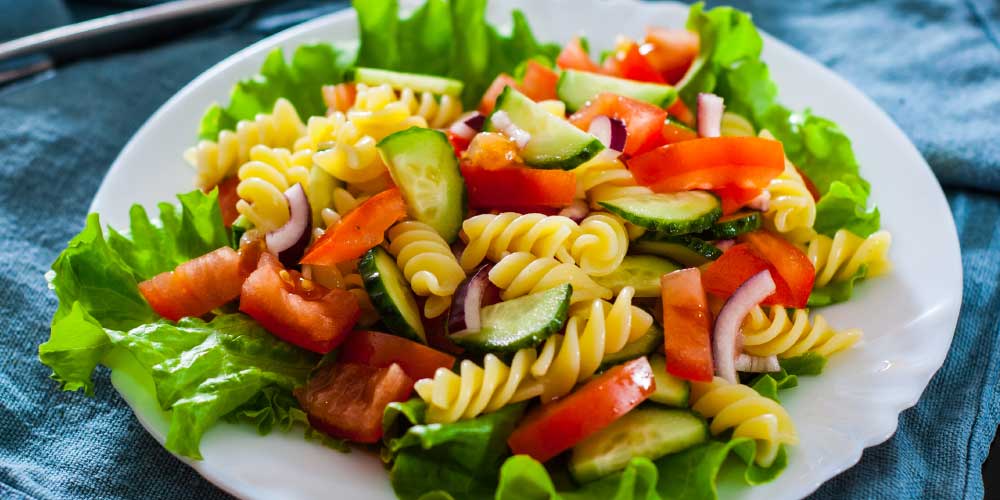Summertime pasta salad with cucumber, tomato, and red onion over lettuce