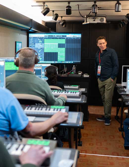 Three participants use pad controllers in the foreground while a facilitator stands by a screen