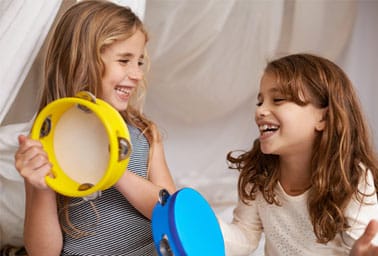Two smiling girls play a yellow tambourine together during an instrument discovery activity