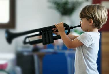 A young boy plays a trumpet indoors during an instrument discovery activity