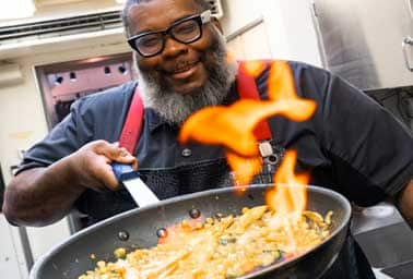 A chef flambés a skillet of food at a community event cooking demonstration