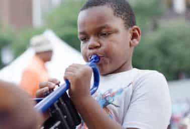 Child plays a blue plastic horn with focused expression during an instrument discovery event