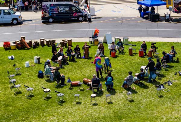 Overhead view of a large drum circle on a grassy field beside the Mobile Music Lab van