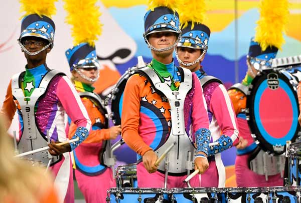 Marching band drummers in colorful uniforms and plumed helmets perform with snare drums
