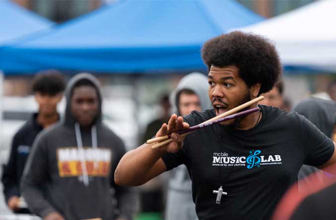 A Mobile Music Lab staff member holds drumsticks while directing a group of students outdoors