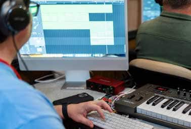 Musician in headphones edits a waveform on a computer screen next to a MIDI keyboard
