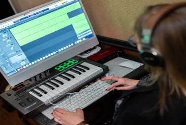 Person wearing headphones plays a MIDI keyboard in front of a digital audio workstation screen